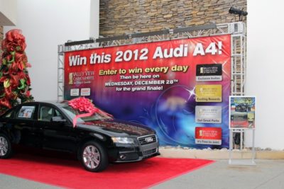 Banner advertising a 2012 Audi A4 giveaway, featuring a black car with a red bow, vibrant colors, and promotional text emphasizing daily entries and a grand finale event.