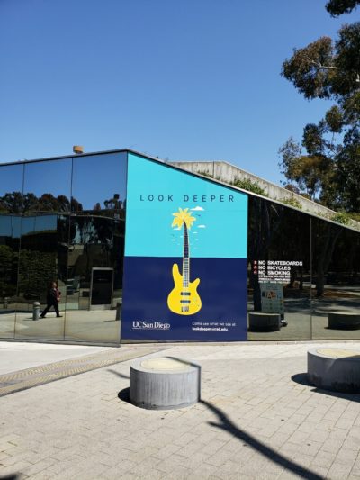Building mural featuring a yellow guitar and palm tree with the text "LOOK DEEPER" and "UC San Diego," enhancing urban aesthetics and brand identity.