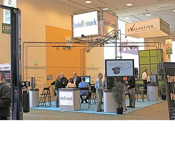 Trade show display booth featuring "intelli mark" branding, with attendees interacting and engaging at various stations, showcasing design elements for effective brand presence at events.