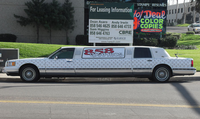 Limousine adorned with automotive window decals featuring "858 Graphics" branding, showcasing creative vehicle customization in an urban setting.