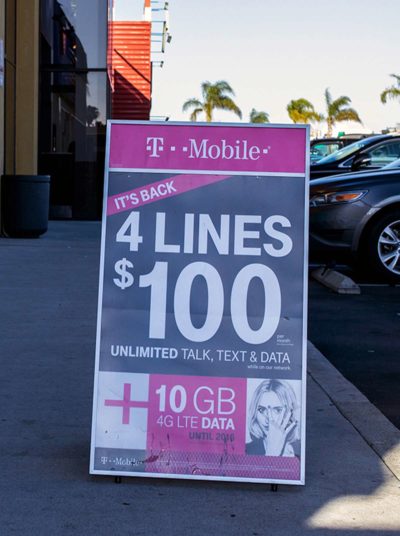 A-frame sign advertising T-Mobile promotion for four lines at $100, featuring unlimited talk, text, and data, with additional 10 GB 4G LTE data offer.
