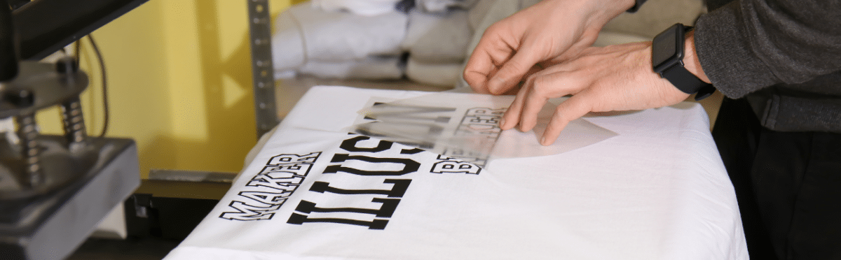 Hands applying a design to a white T-shirt using a heat press, showcasing custom printing techniques relevant to branding and promotional items.