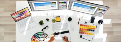 Creative workspace with dual monitors displaying design software, color palette, sketching tools, and a hand drawing, emphasizing custom metal outdoor sign design and branding solutions.