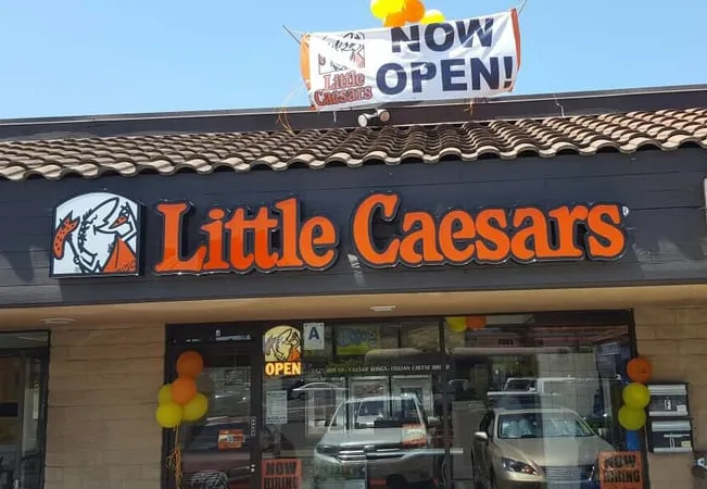Little Caesars restaurant exterior with "NOW OPEN!" banner and colorful balloons.